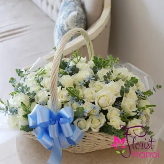 100 white rose arrangement in a woven basket with fresh eucalyptus