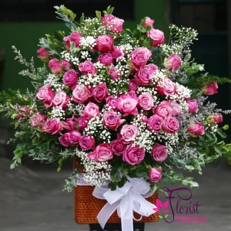 Purple rose mix baby flower arrangement in a wicker basket with fresh baby's breath and greenery
